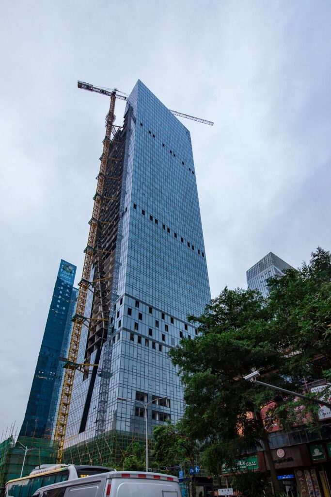 Modern skyscraper under construction with cranes in a bustling urban area.