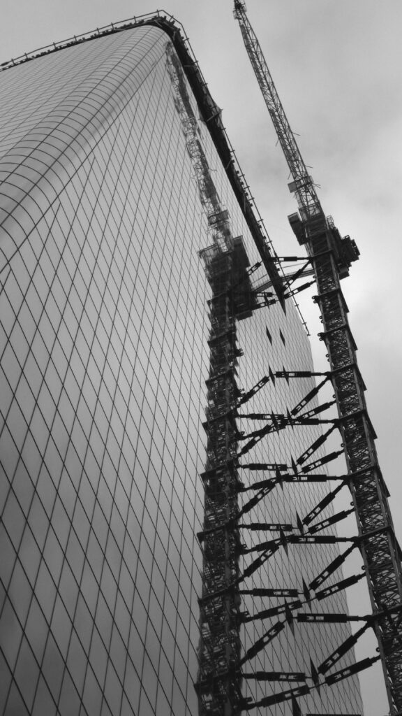 pexels-photo-1702140-1702140 Low angle view of a skyscraper under construction with cranes, captured in monochrome.