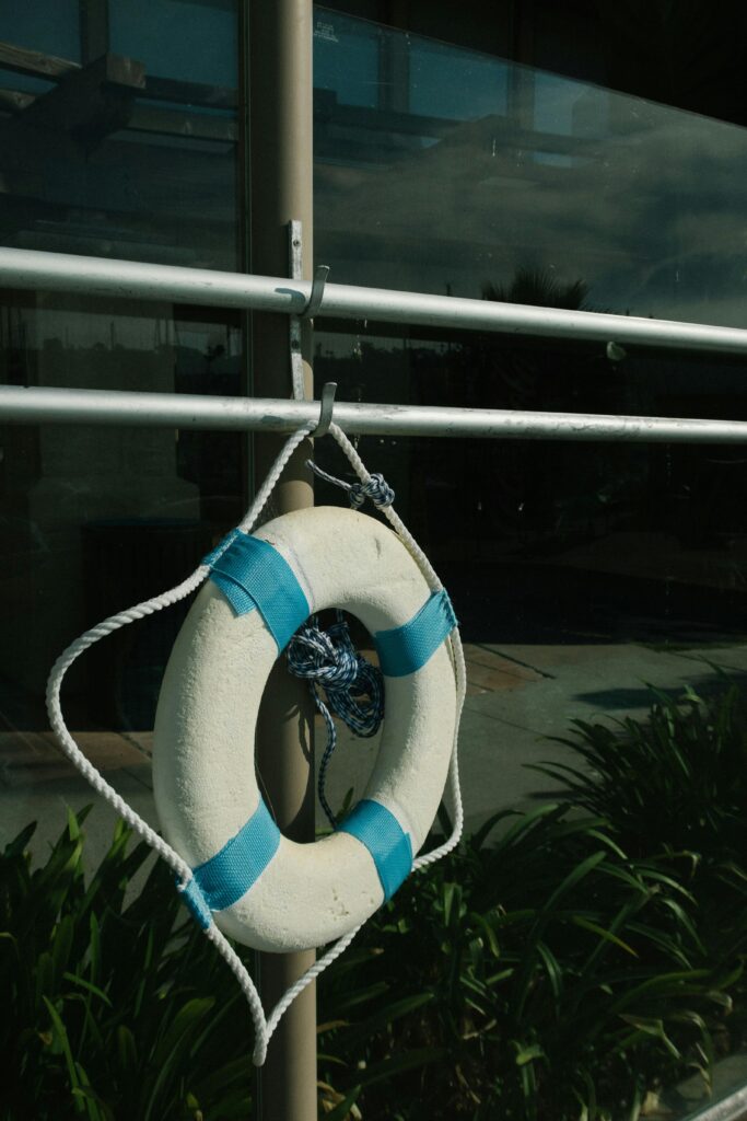 A white lifebuoy with blue stripes hanging outside on a metal frame by a window.